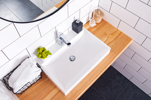 flat-lay view of bathroom sink with white towels in black wire basket against white tiling